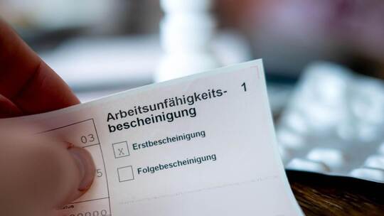 Eine Person hält eine Arbeitsunfähigkeitsbescheinigung