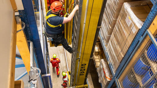 Ersthelfer Guido Möller erklimmt die Leiter eines Hochregallagers, um den „Patienten“ Marcel Praßl (in der Fahrkabine) zu bergen Einsatzübung Höhenrettung Hochregallager