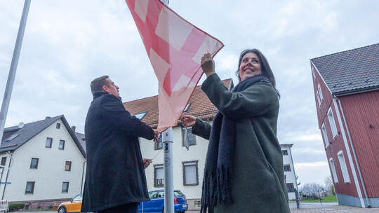 Bürgermeister Thomas Keller und Assistentin Kim Bechtle hissen die Fahne, die als Symbol gegen Gewalt an Frauen in der Ortsmitte Engelsbrand Fahnenaktion Gegen Gewalt an Frauen