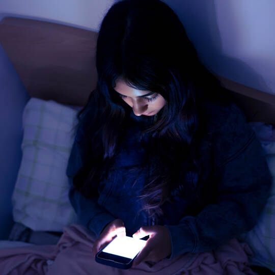 Sad and tired teenager girl using a smartphone lying in bed late at night, playing games, watching videos, and typing. Children'