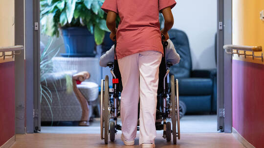Eine Bewohnerin eines Pflegeheims wird von einer Pflegerin einen Gang entlang geschoben. Nicht überall werden Pflegebedürftige g Pflegerin und Patientin (Symbolbild)