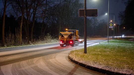 Ein Streufahrzeug in streut auf einer Straße. Ein Streufahrzeug in streut auf einer Straße.