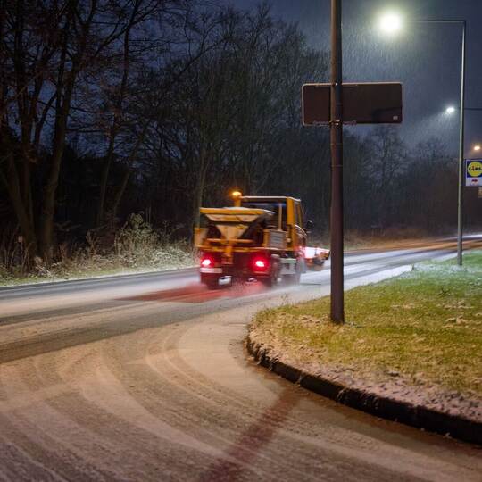Ein Streufahrzeug in streut auf einer Straße. Ein Streufahrzeug in streut auf einer Straße.