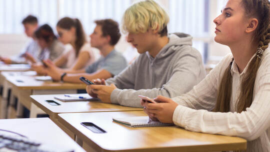 Teen students using social media on phones on lesson