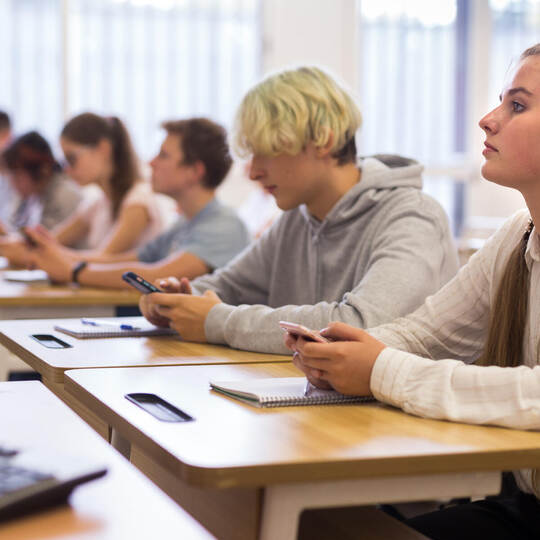 Teen students using social media on phones on lesson