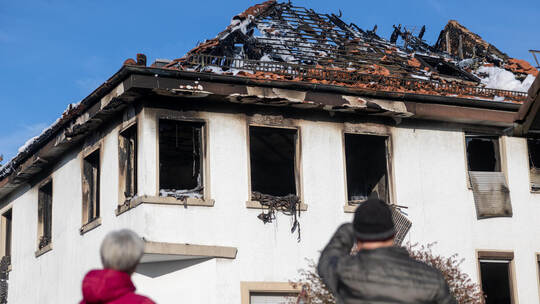 Voll Mitgefühl betrachten zwei Passanten das Brandhaus an der Ecke Brötzinger/-Schulerstraße in Büchenbronn.