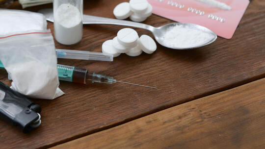 A lot of narcotic substances pills and devices for the preparation of drugs lie on an old wooden table