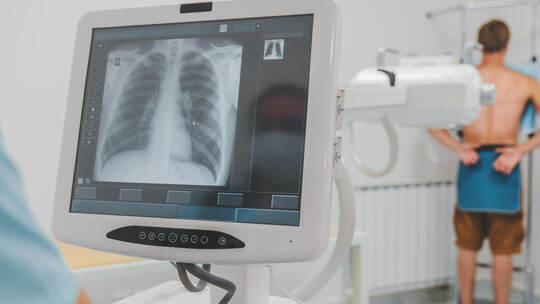 Young caucasian man standing against wall while doctor using X-Ray machine scan him in hospital