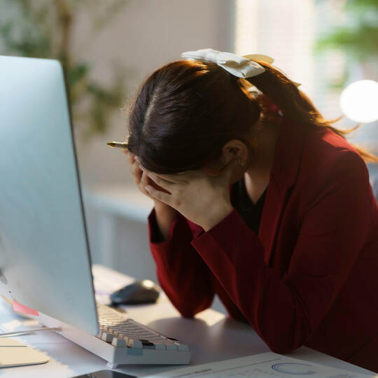 Young businesswoman is sitting at her desk with her head in her hands, suffering from a headache after working on a computer