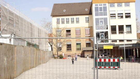 Eingezäunter Hof der Grundschule: Im Vergleich zur vorigen Pausen-Situation, als die Fläche hinter dem Holz-Bauzaun noch unbebau