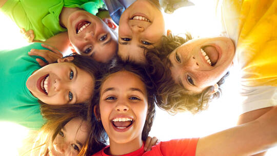 Group of happy little children playing together, having fun, huddling, looking down and smiling