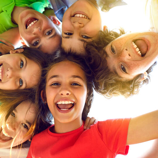 Group of happy little children playing together, having fun, huddling, looking down and smiling