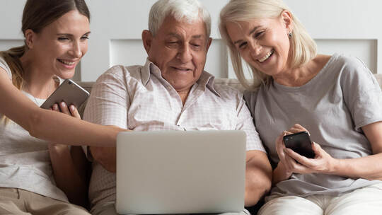 Happy older parents with adult daughter using electronic devices