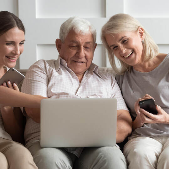 Happy older parents with adult daughter using electronic devices