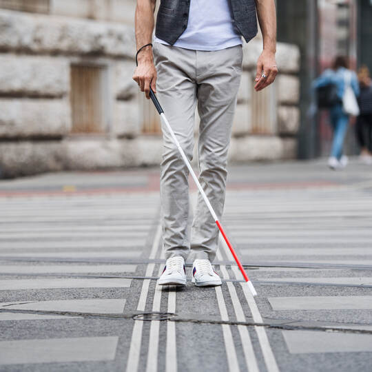 Midsection of young blind man with white cane walking across the street in city.