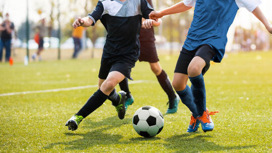 Two soccer players running and kicking a soccer ball. Legs of two young football players on a match. European football youth pla