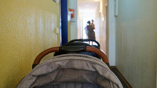 In einem Frauenhaus stehen Kinderwagen im Flur, während eine Mutter mit ihren Kindern am Ende des Flurs entlanggeht. In Pforzhei Frauenhaus in Deutschland