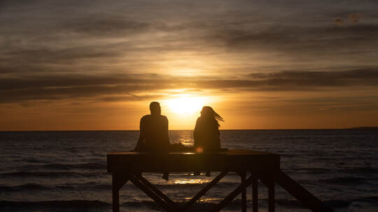 Paar sitzt bei Sonnenuntergang am Strand von Arenal