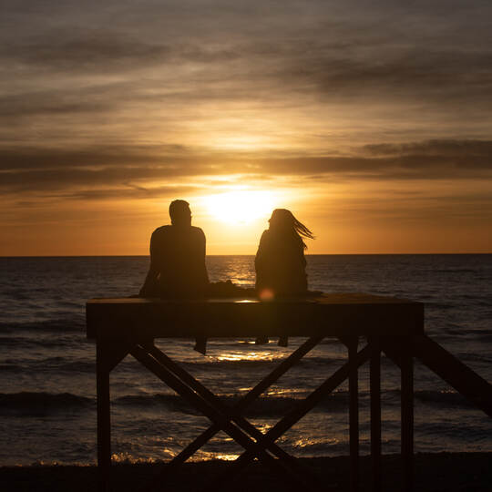 Paar sitzt bei Sonnenuntergang am Strand von Arenal