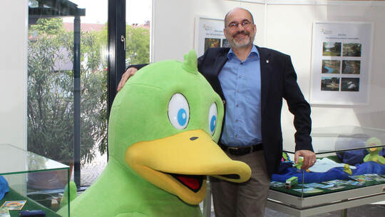 Bürgermeister Armin Dauner und das quietschgrüne Maskottchen „Enzle“ im Rathaus Mühlacker bei der kleinen Ausstellung, die im Fo