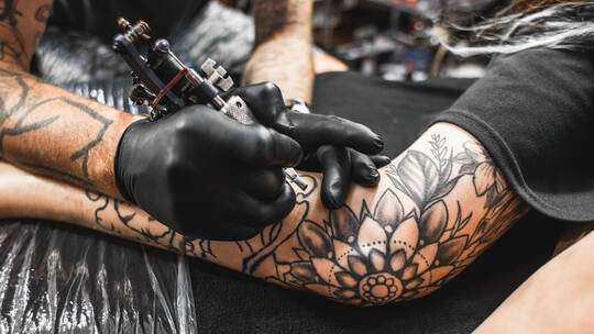 girl with dreadlocks in a tattoo parlor. The master creates a picture on the body of a young beautiful girl. Close-up of hands a