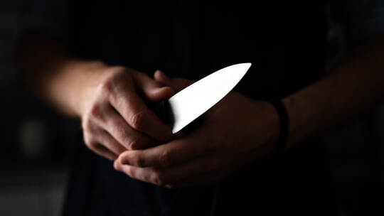 Man Holds Sharp Kitchen Knife in black room