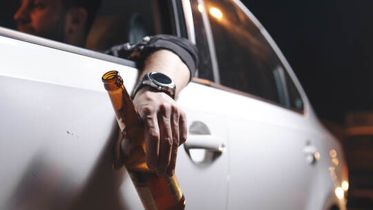 Drunk young man drives a car with a bottle of beer. This is a campaign picture of Don't Drink for Drive.