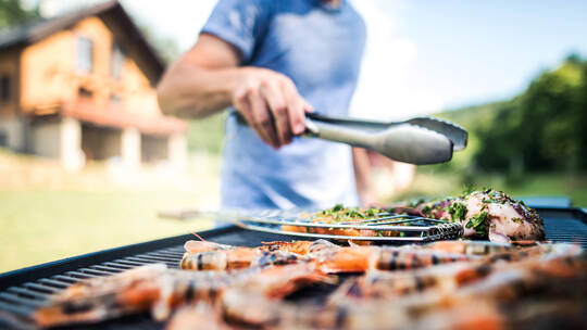 Unrecognizable man cooking seafood on a barbecue grill in the backyard.
