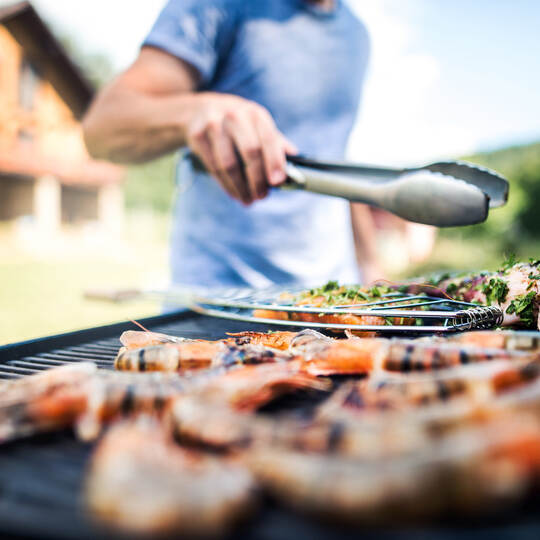 Unrecognizable man cooking seafood on a barbecue grill in the backyard.