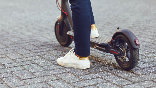 Young man in a helmet rides an electric scooter on a city street in summer