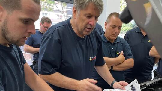 Mit dem Plan in der Hand studieren die Berufsfeuerwehrleute das Innenleben eines SUV Cupra Tavascan in der Werkstatt von Hahn Au