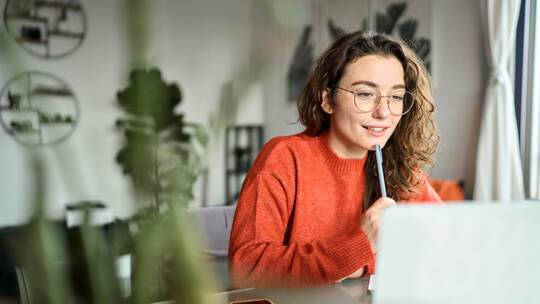 Young smiling woman student using laptop watching webinar writing at home.