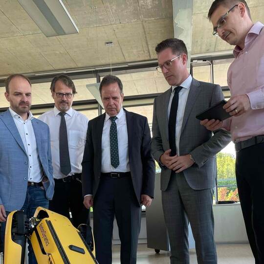 Der Roboterhund reckt und streckt sich, was fasziniert beobachtet wird von: CDU-Landtagskandidat Andreas Renner, Professor Raine