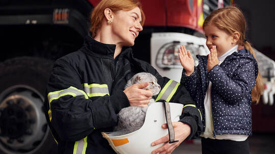 Mit dem Preis werden Menschen geehrt, die Besonderes leisten. stock.adobe.com Cat is sitting in the helmet, kid is happy, clapping her hands. Firefighter woman in uniform is with a little girl