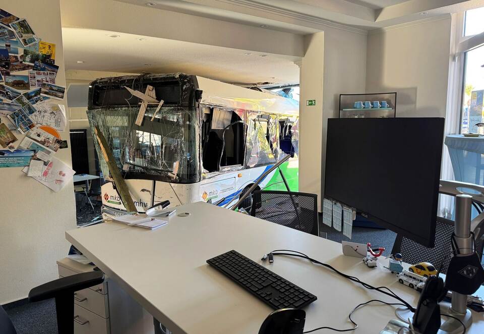 Bus kollidiert mit Auto und kracht in Reisebüro