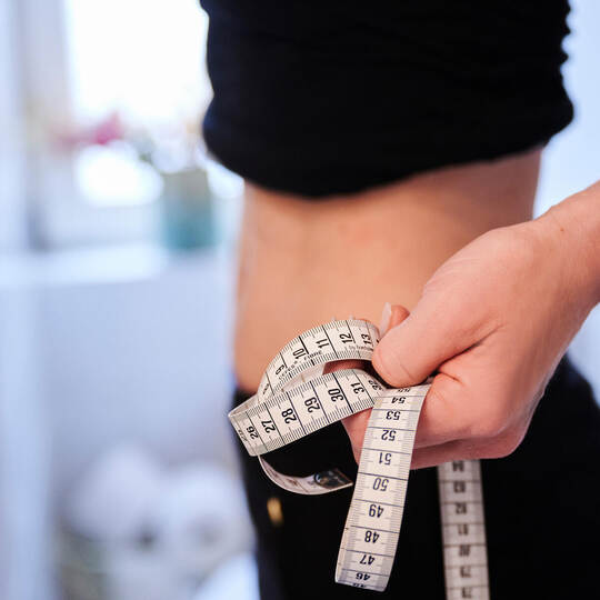 Eine junge Frau hält ein Zentimetermaßband an ihren Bauch