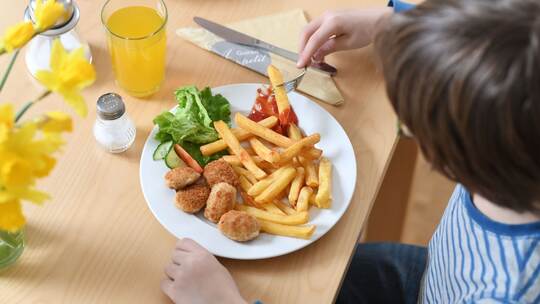 Ein Kind isst Chicken Nuggets und Pommes Frites