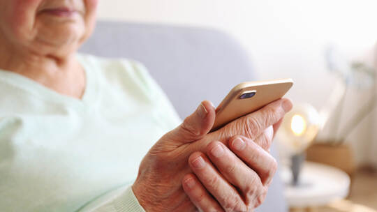 Elderly woman holding blank screen cell phone gadget in hands. Old lady with wrinkled skin trying to vigure out touchscreen smar