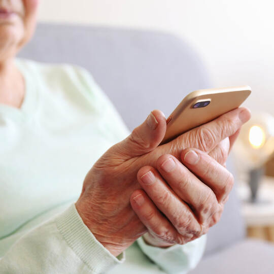 Elderly woman holding blank screen cell phone gadget in hands. Old lady with wrinkled skin trying to vigure out touchscreen smar