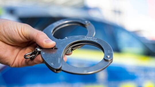 Handschellen vor Polizeiwagen - Symbolbild Handschellen vor Polizeiwagen - Symbolbild