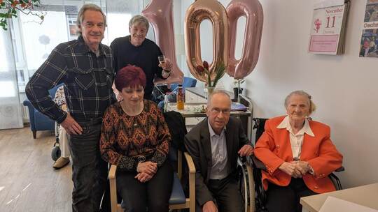 Bürgermeister Frank Fillbrunn (kniend) überbringt Geburtstagskind Margarete Ernst (rechts) Geburtstagsgrüße von Ministerpräsiden