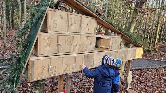 Vor dem großformatigen Adventskalender erleben Kinder den besonderen Zauber des Weihnachtswalds, der mit liebevoll gestalteten D