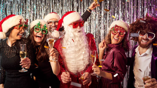 Happy people standing together with a man in Santa Claus costume celebrating New Year's Eve party