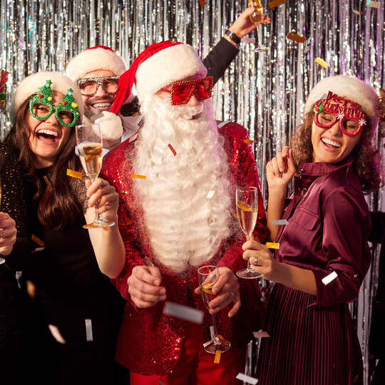 Happy people standing together with a man in Santa Claus costume celebrating New Year's Eve party
