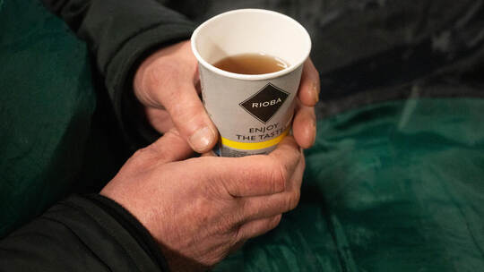 Ein Obdachloser hält einen Becher Tee in der Hand, um sich bei den kalten Außentemperaturen aufzuwärmen. Christophe Gateau/dpa Obdachloser