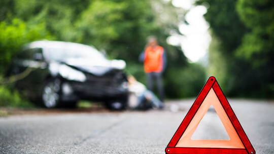 A close up of a red emergency triangle on the road in front of a car after an accident.