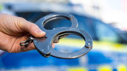 Handschellen vor Polizeiwagen - Symbolbild