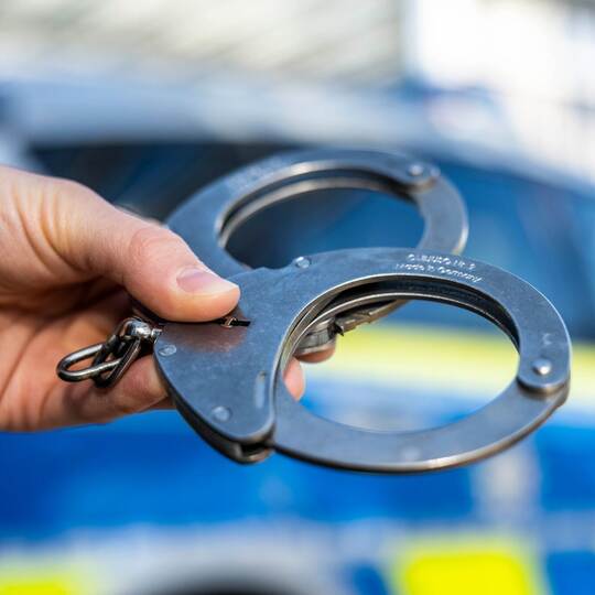 Handschellen vor Polizeiwagen - Symbolbild