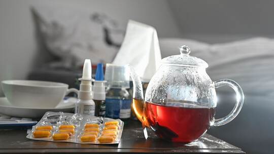 Medikamente und eine Kanne Tee auf einem Nachttisch