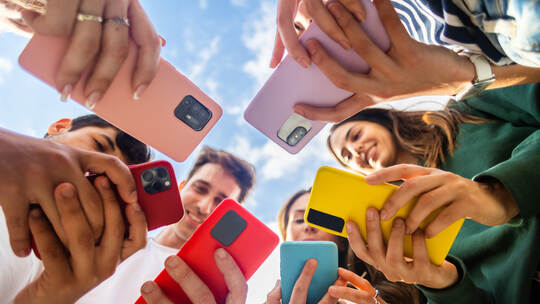 Young group of people using mobile phone device standing in circle outdoors